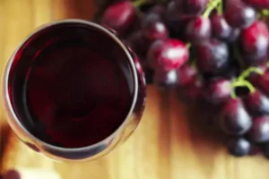 Rotweinglas von oben auf Holzbrett. Rechts davon rote Weintrauben.