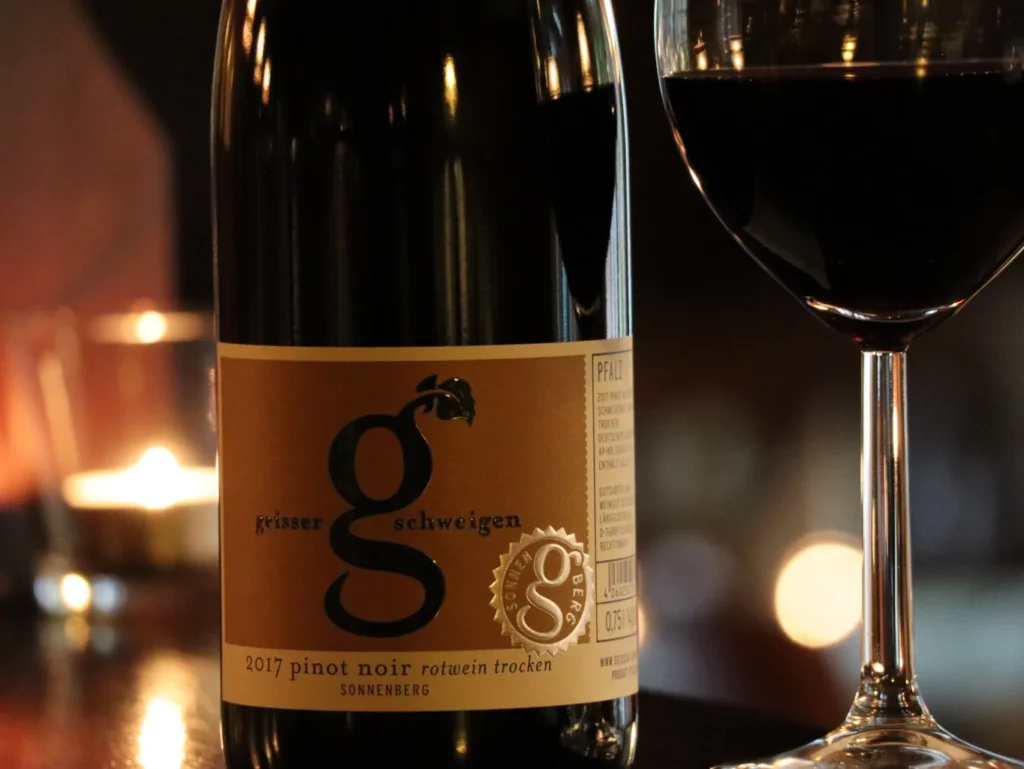 Geisser Pinot Noir Sonnenberg trocken Weinflasche mit Weinglas. Im Hintergrund Kerzenlicht.